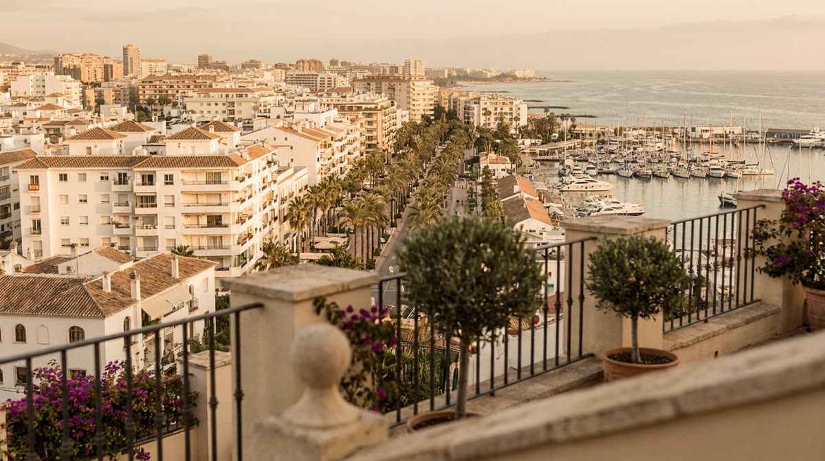 Vista al atardecer sobre una ciudad costera española con edificios de apartamentos, palmeras y puerto deportivo